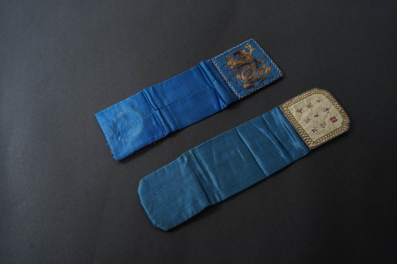 Two Chinese late Qing Dynesty coloured silk and gold thread embroidered belt purses, or ‘hebao’, for carrying coins, seals and fragrant herbs etc. One - 19cm long,in cream silk, with the embroidered words: “It’s music is